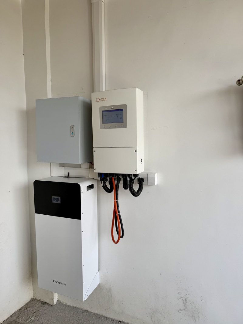 The finished equipment wall: inverter beside the protection box, battery below, cables in conduit.