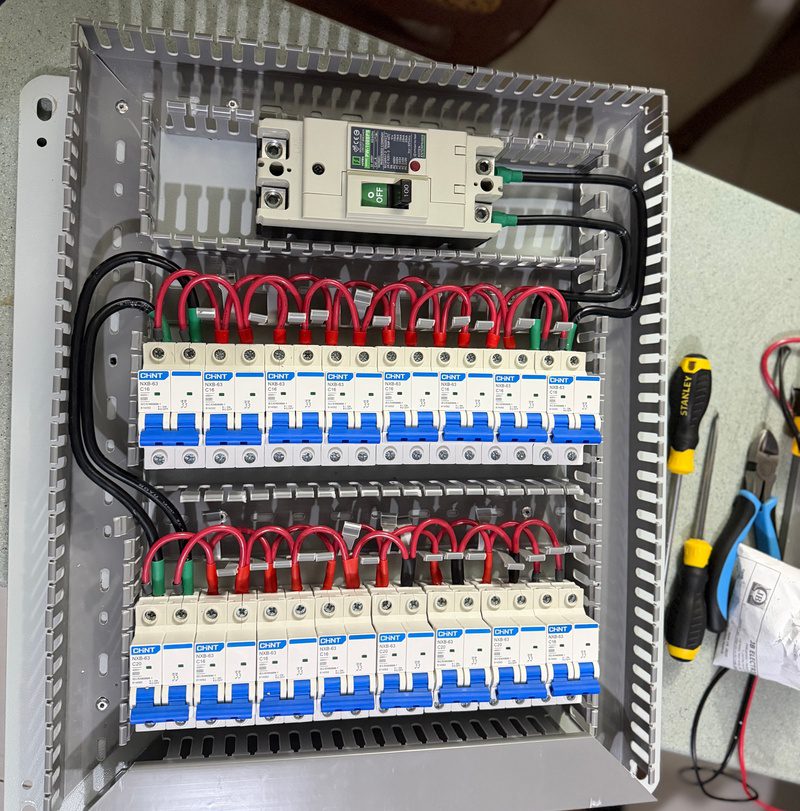 A distribution board being assembled on the bench: main breaker on top, two rows of circuit breakers with red jumpers.